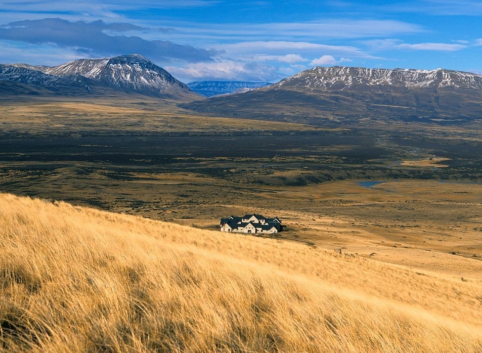 Wide view of Eolo lodge surrounded by grassy plains with mountains in the background in Patagonia