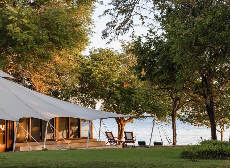A large white luxury tent with a wooden deck and chairs facing the calm sea at Amanwana.