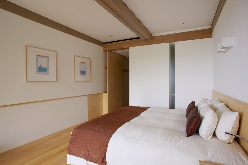 Interior of a minimalist bedroom with white walls, light wood trim, a double bed and two framed art pieces.
