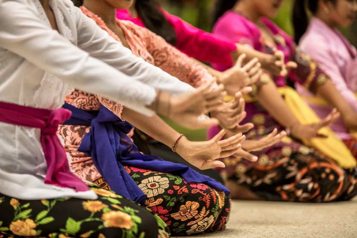 A close-up profile view of dancers in bright clothing performing expressive hand movements during a traditional Balinese dance.