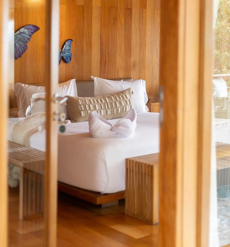 View through glass doors of one of Delfin I's bedrooms with a white bed, wooden panelling, and blue butterfly wall decor.