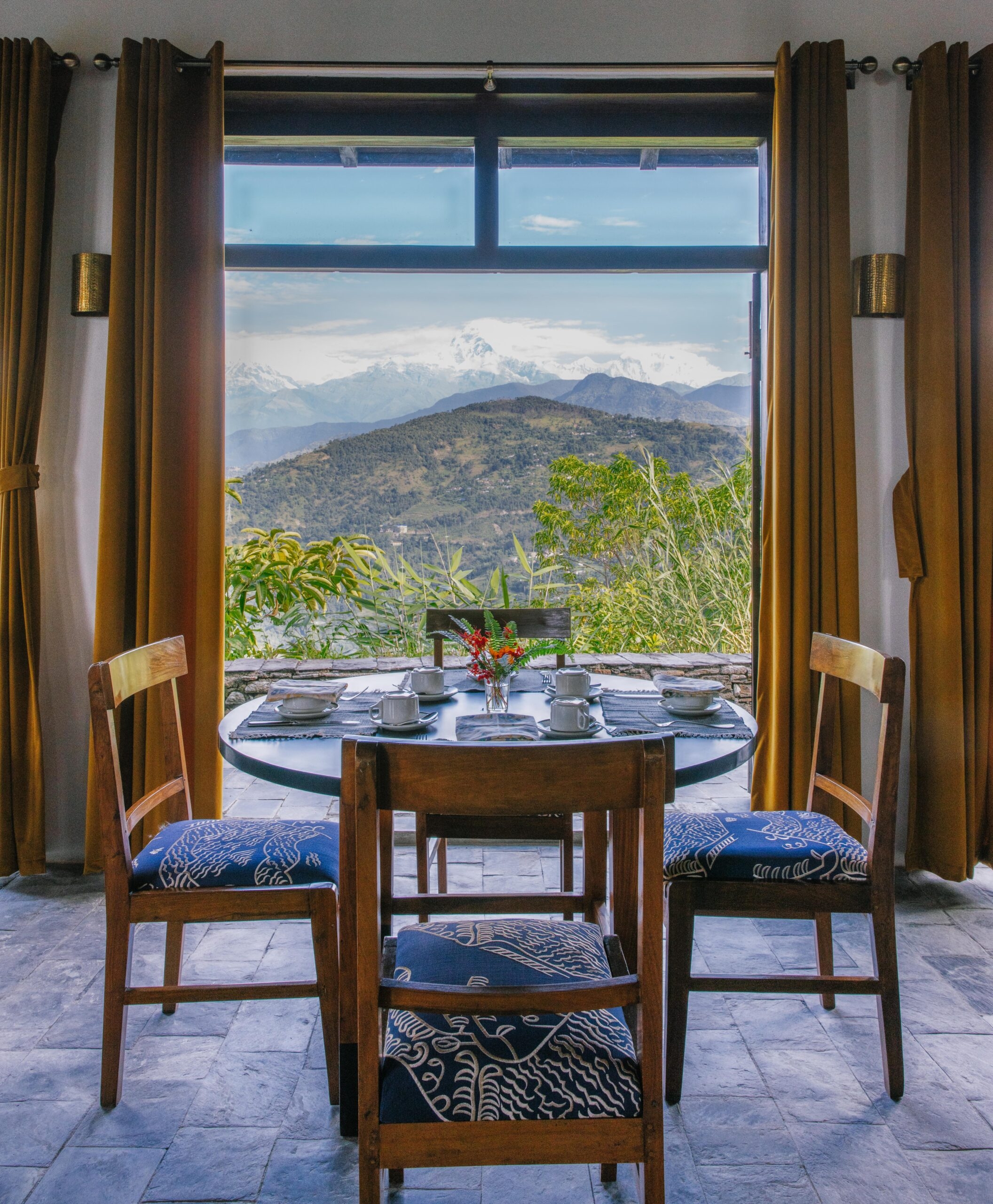 Dining table with chairs facing a window revealing a scenic mountain view.