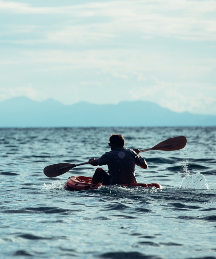 A person kayaking on a calm sea with mountains in the distance.