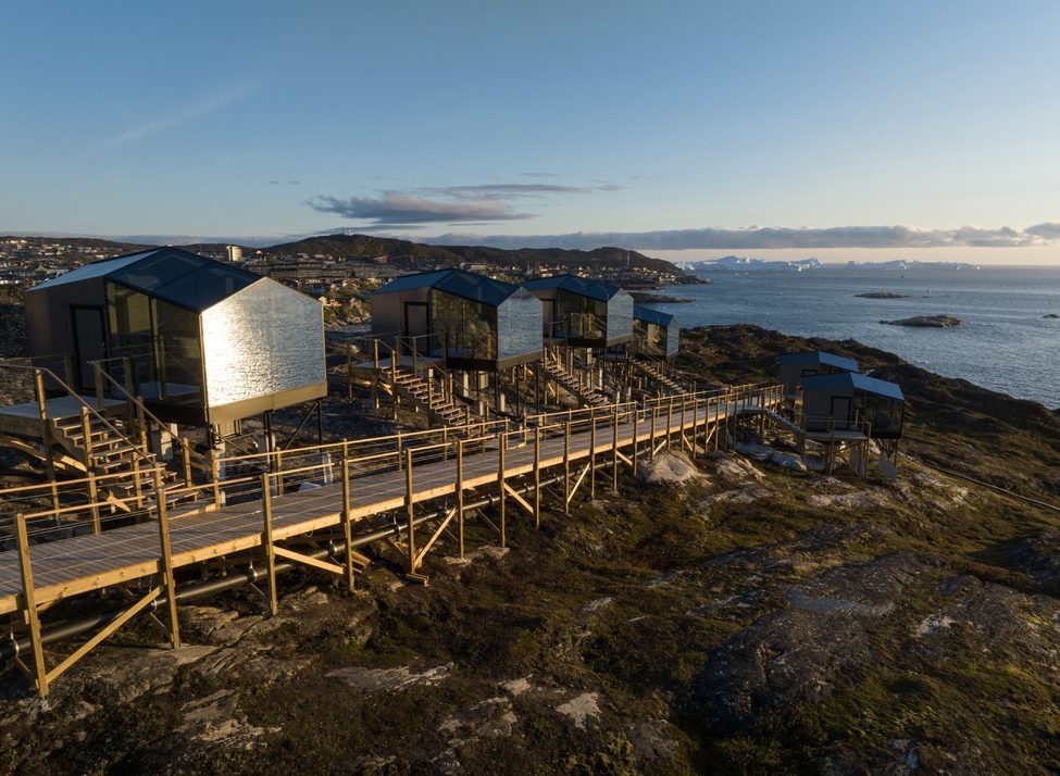 Glass and wood huts on a rocky shore reflecting the sea at Hotel Arctic in Greenland