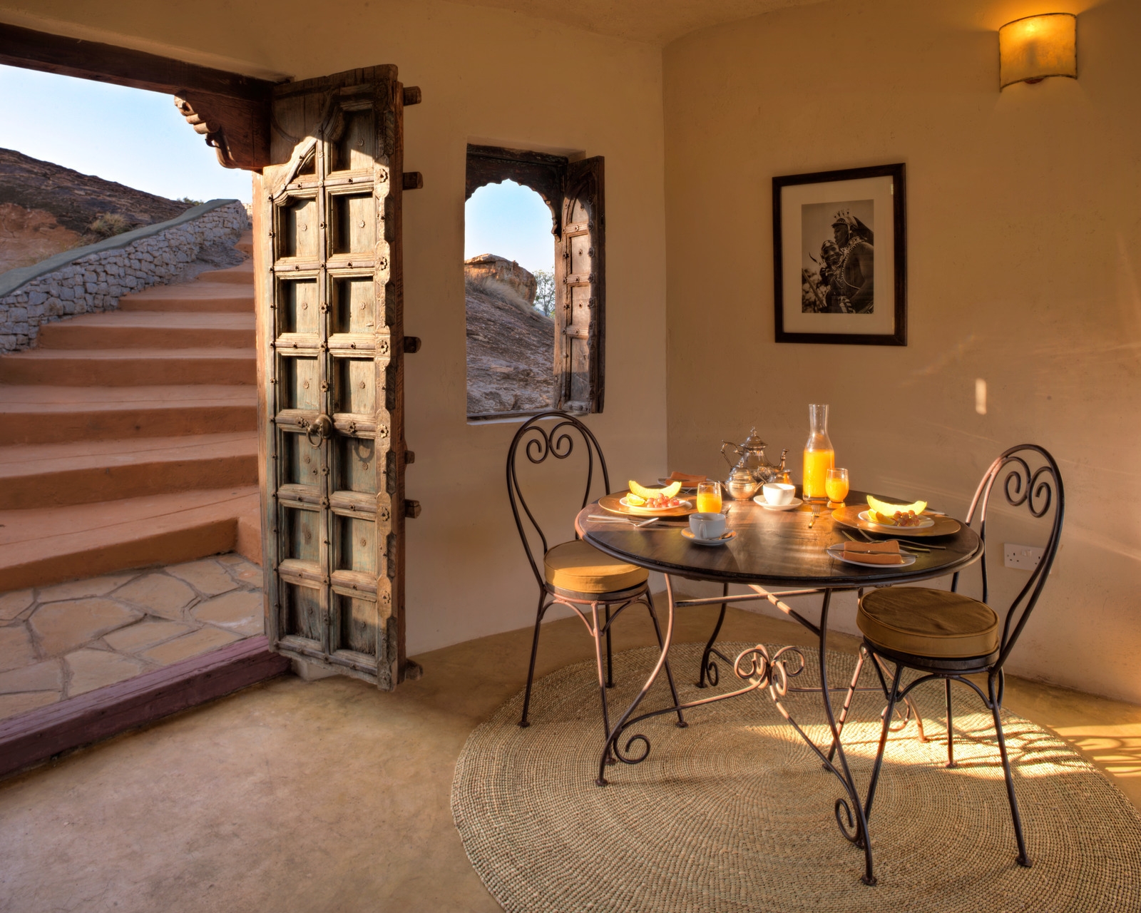 A breakfast setting for two inside a room with a carved wooden door opening to stone steps at Saruni Samburu.