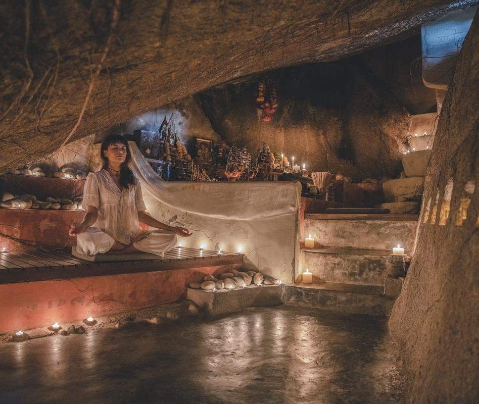 A woman meditating inside a candlelit stone cave.