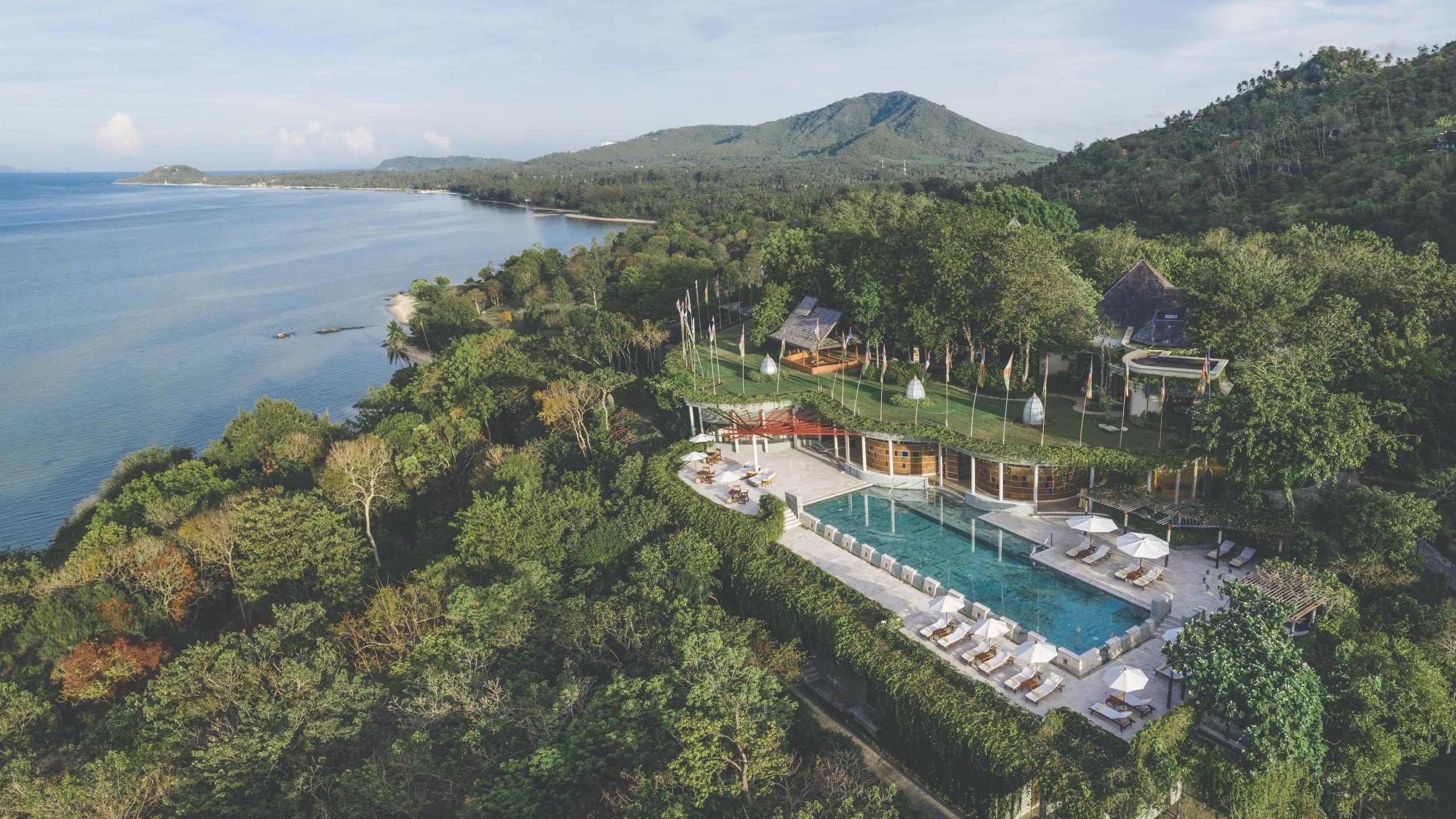 Aerial view of Kamalaya surrounded by lush green trees next to the coastline.
