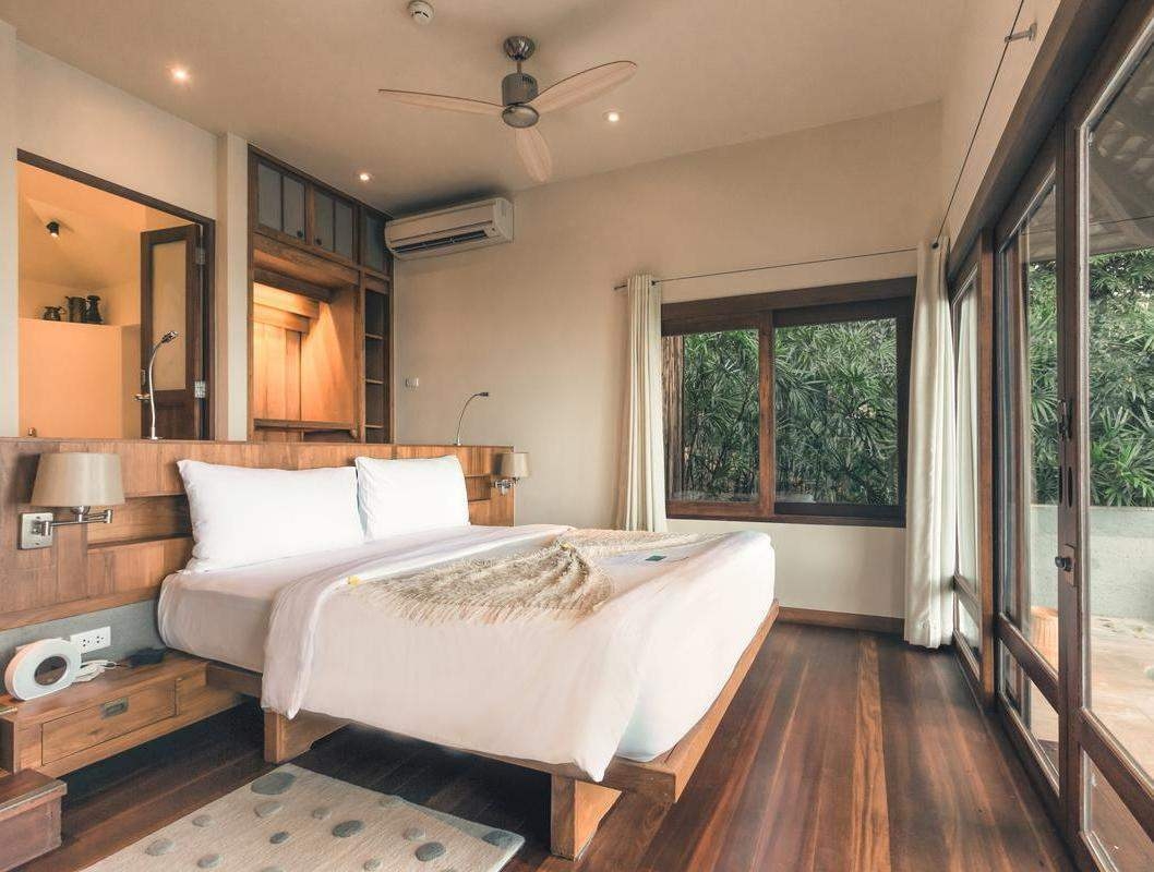 Tropical villa bedroom with a large white bed, wooden floors and large glass doors.