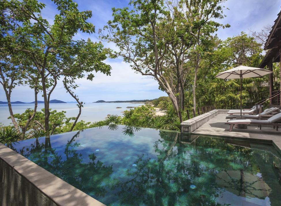 Infinity swimming pool with a scenic ocean view, surrounded by tropical trees and patio lounge chairs.