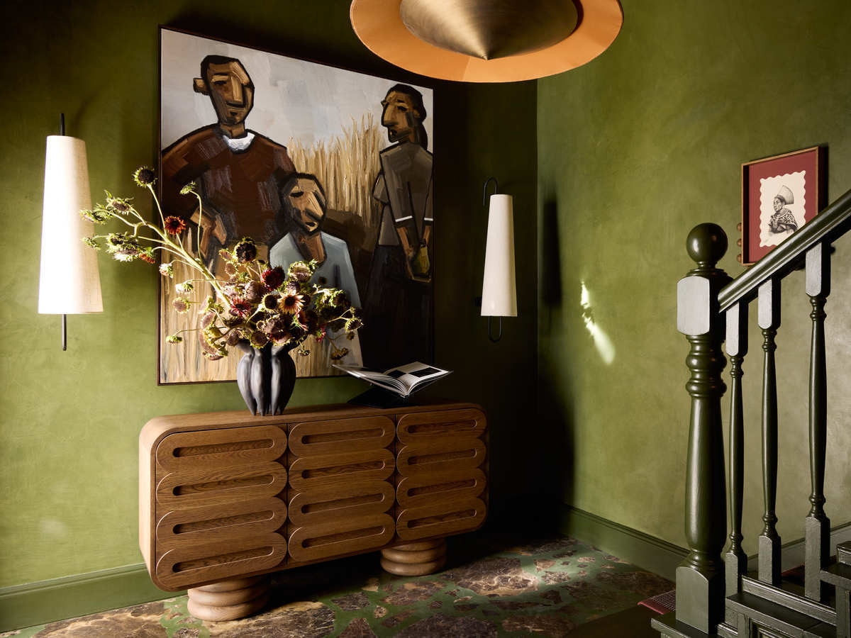 Olive green room featuring a mid-century wooden console, a large portrait painting, and stylish white wall sconces.