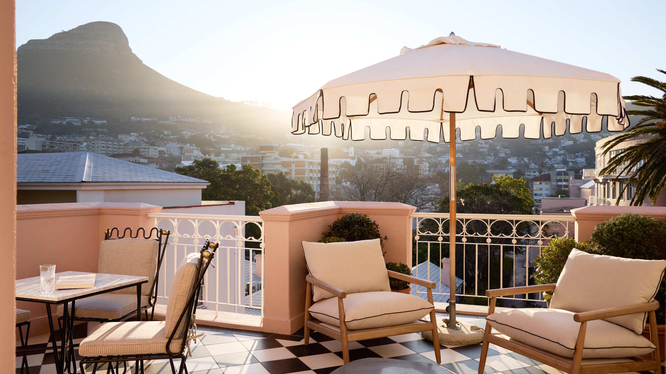 Rooftop terrace with checkered floors, white umbrella, and lounge chairs with Table Mountain in the background.