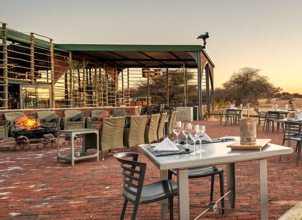 Outdoor dining area with camp fire and metal lodge exterior at Okonjima Plains Camp in Namibia