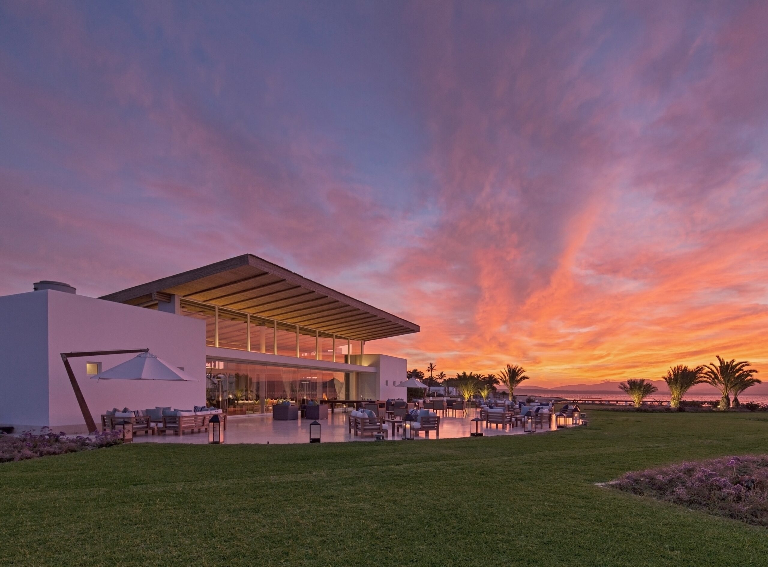 Modern beachfront building at sunset with vibrant sky and palm trees.
