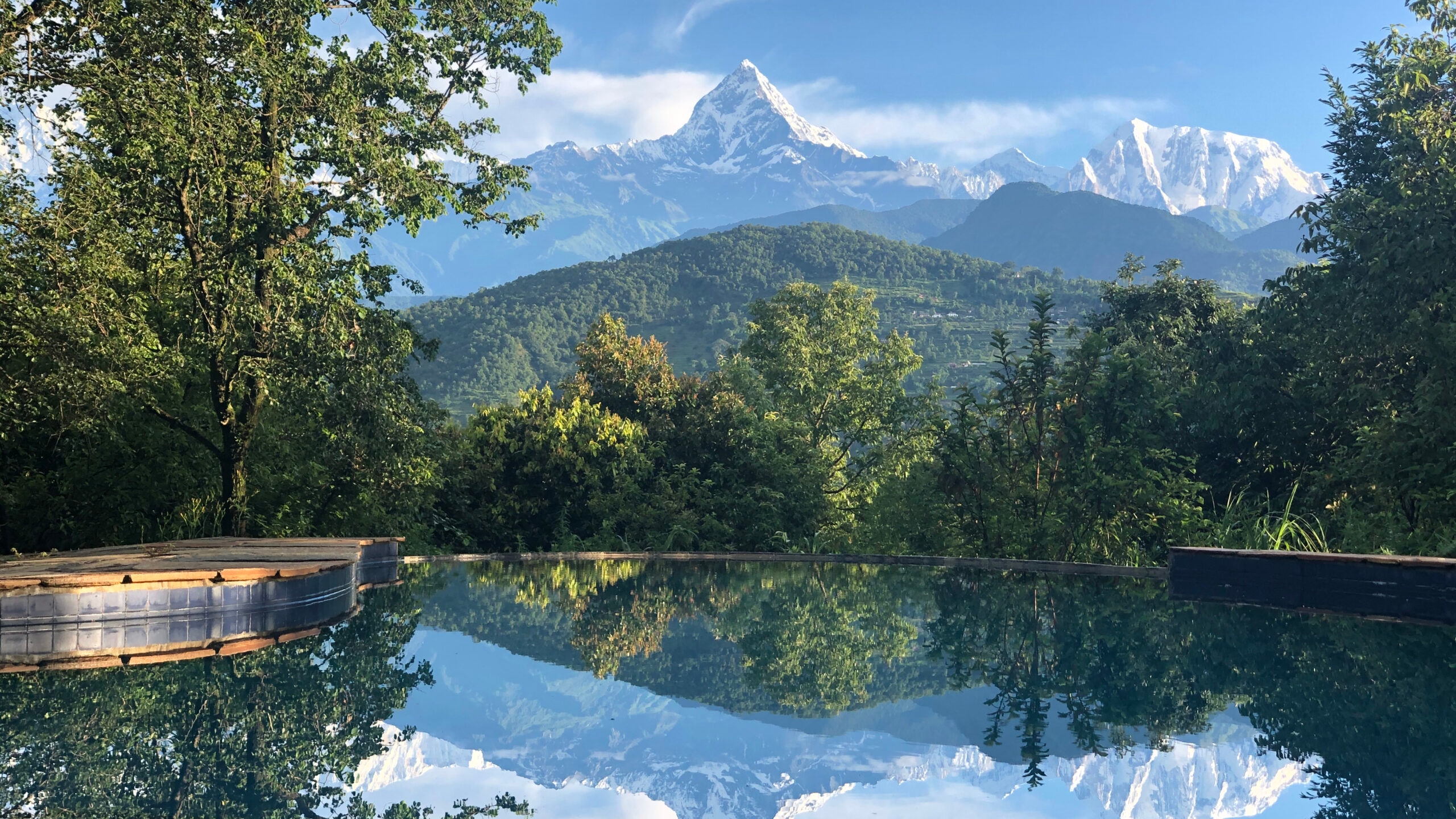 Reflective pool with snowy mountain peaks backdrop, surrounded by vibrant greenery.