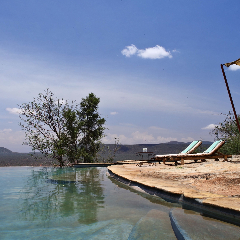 Sun loungers on a stone deck next to a calm swimming pool overlooking the Samburu landscape.