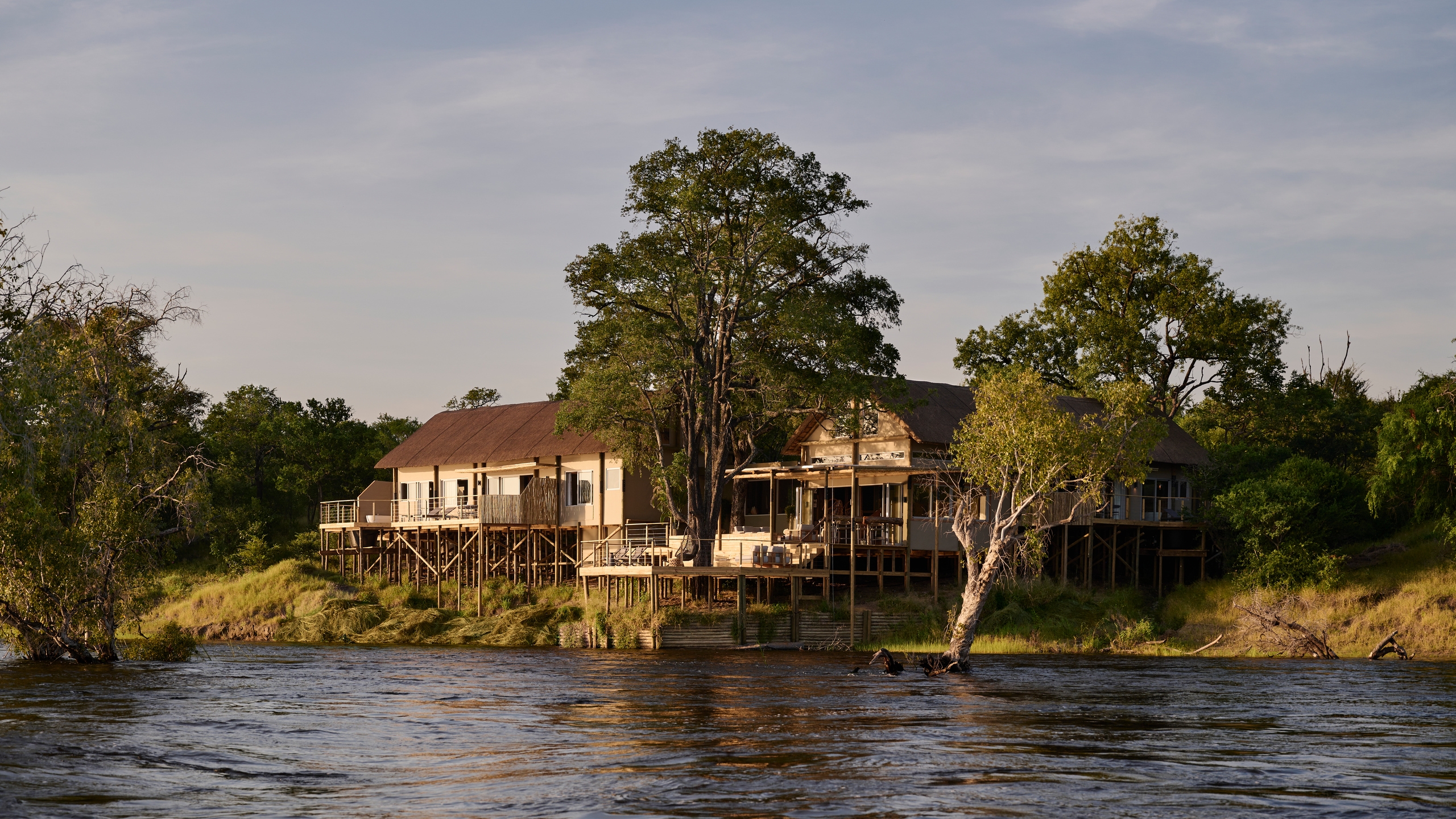 Exterior view of a waterfront villa on stilts at Victoria Falls River Lodge during the golden hour.