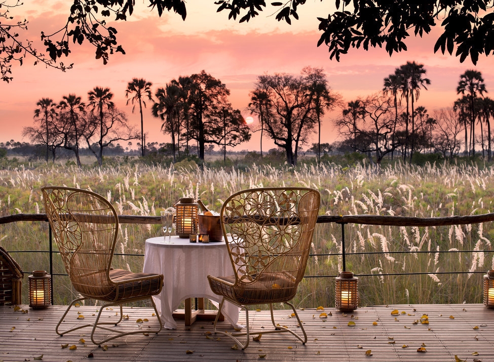 Table for two with champagne and lanterns on a deck overlooking the Botswana savanna at Sandibe Okavango Safari Lodge.