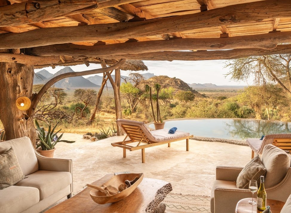 An open-air terrace with white sofas, a wooden table and lounge chairs next to a circular pool with valley views.