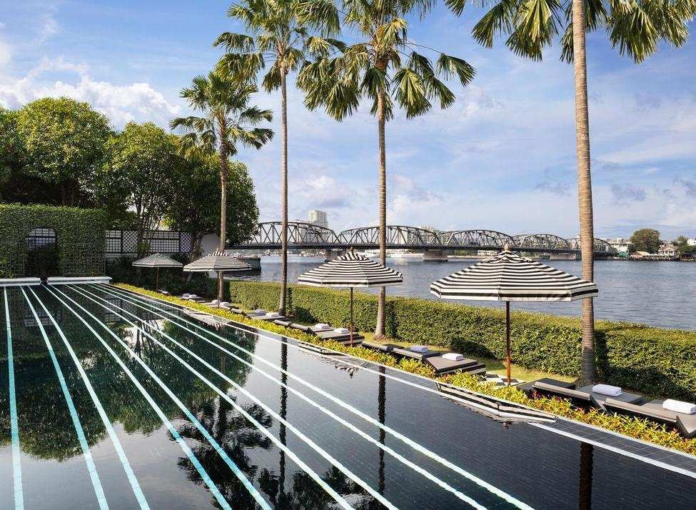 Black tiled infinity pool with white stripes overlooking a river and bridge at the Siam in Bangkok.