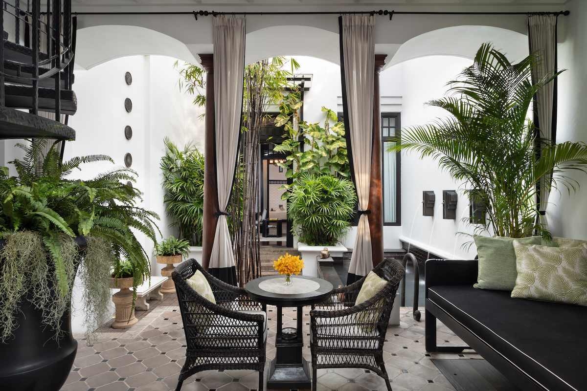 Monochromatic outdoor terrace with black wicker chairs, a small table, and a variety of green potted plants.