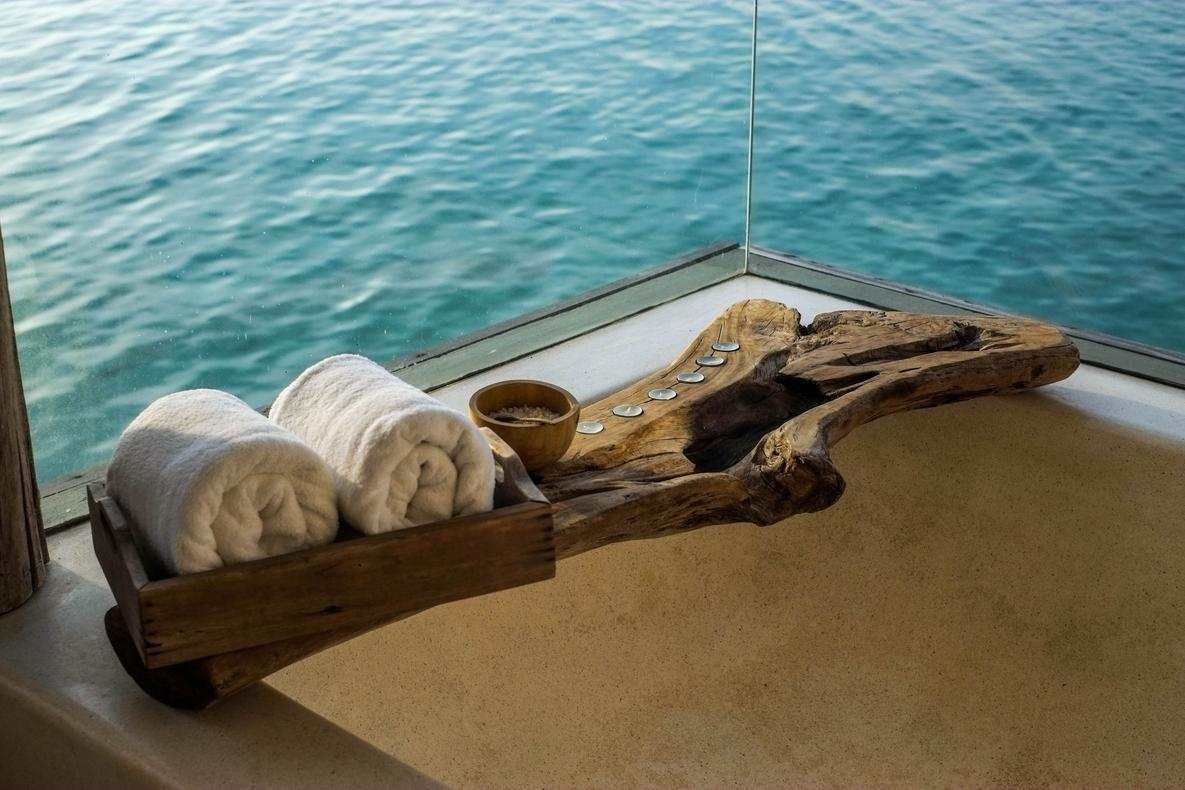 A bathtub with a driftwood tray holding white towels and a small bowl, overlooking the blue ocean.