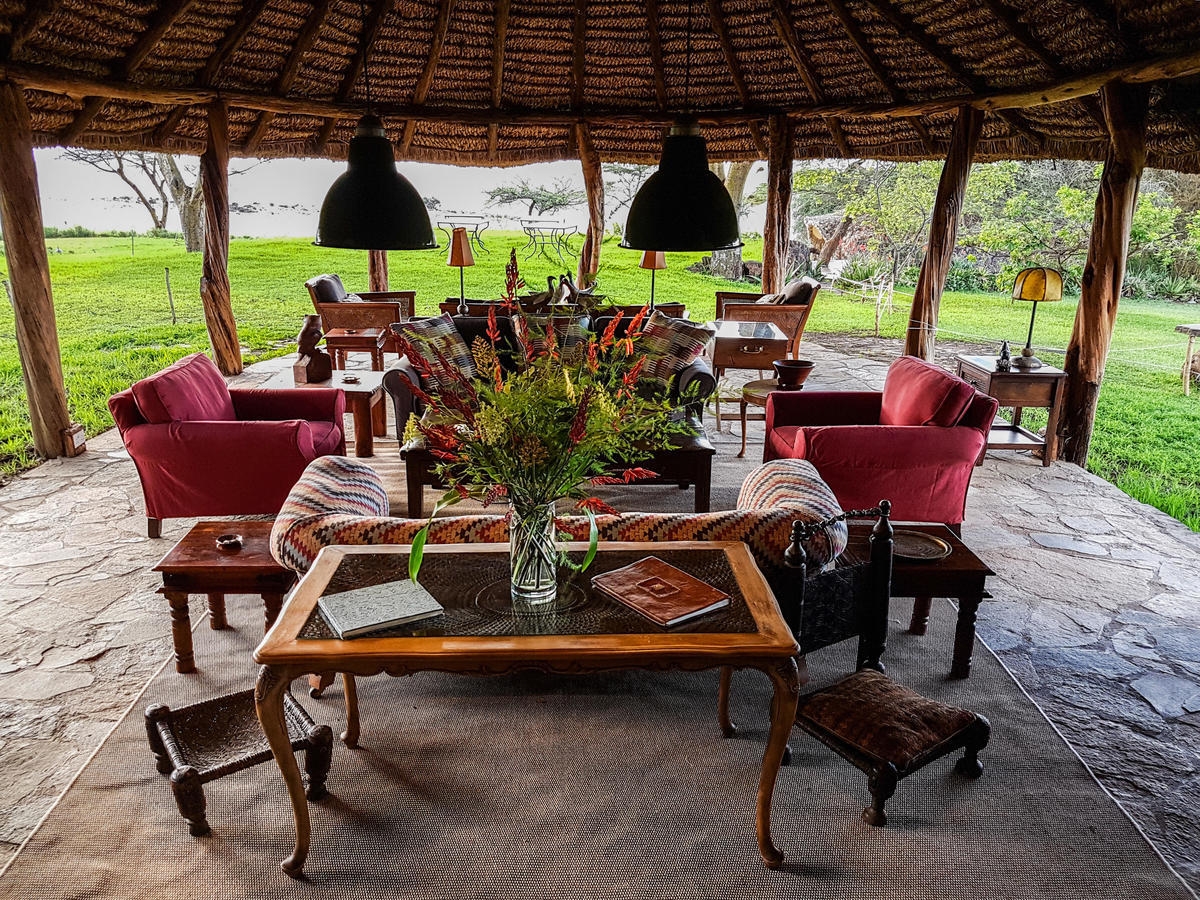 An open-air lounge with red chairs and a thatched ceiling overlooking a green landscape.