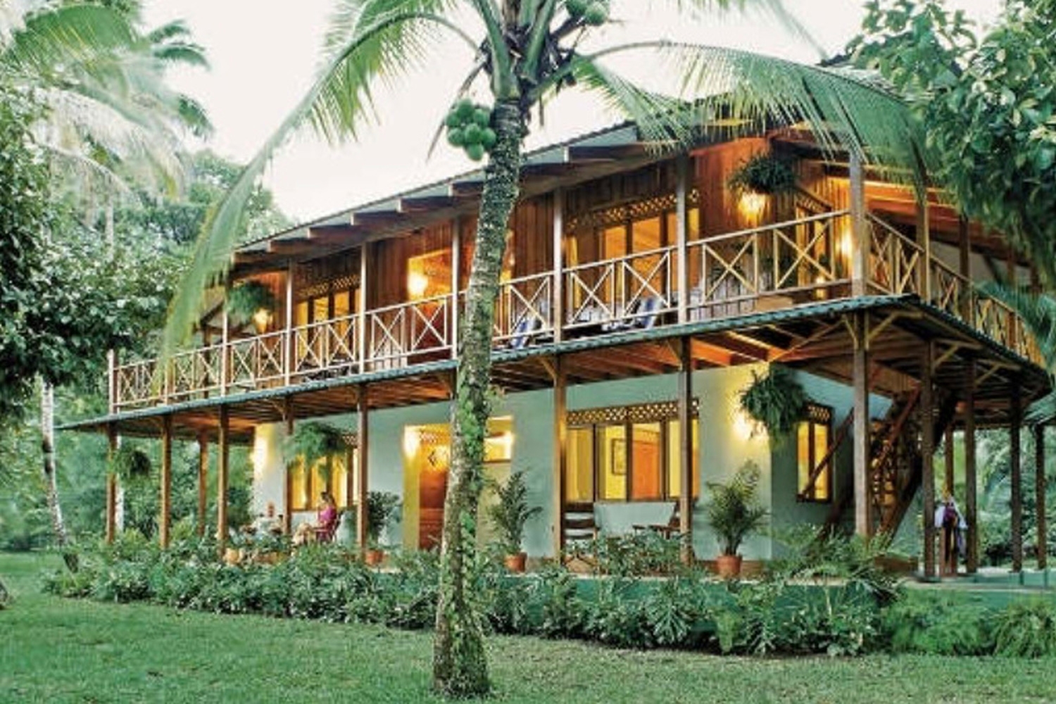 A two-story wooden building with balconies at Tortuga Lodge Costa Rica surrounded by palm trees and tropical plants.