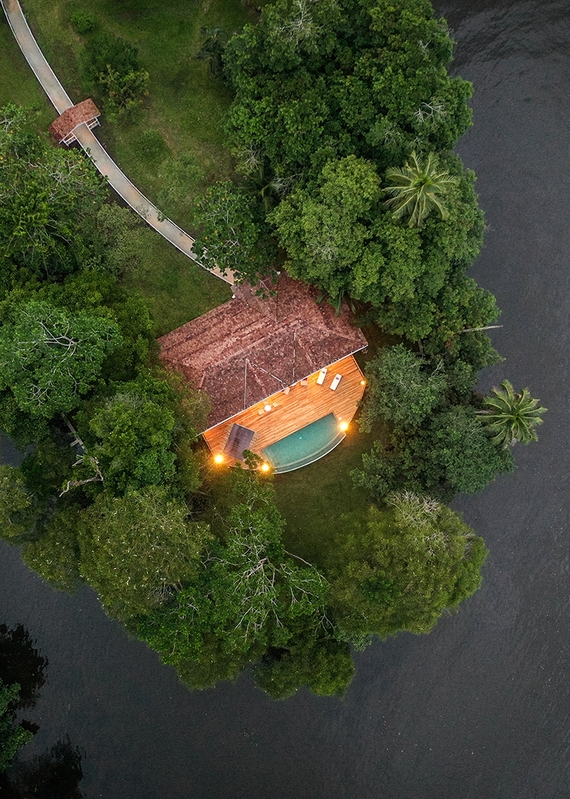 Aerial top-down view of a villa with a glowing swimming pool and wooden deck in the Costa Rican jungle.