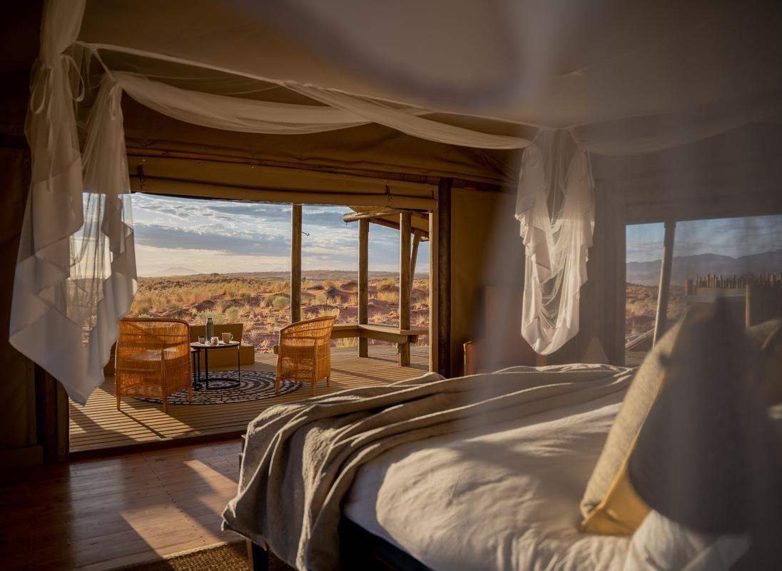 Luxury tented bedroom with white mosquito netting overlooking a sunlit desert landscape.