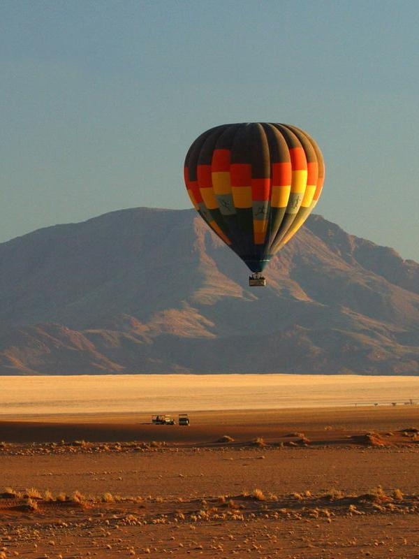 A striped hot air balloon flying over a wide desert plain with mountains in the background.