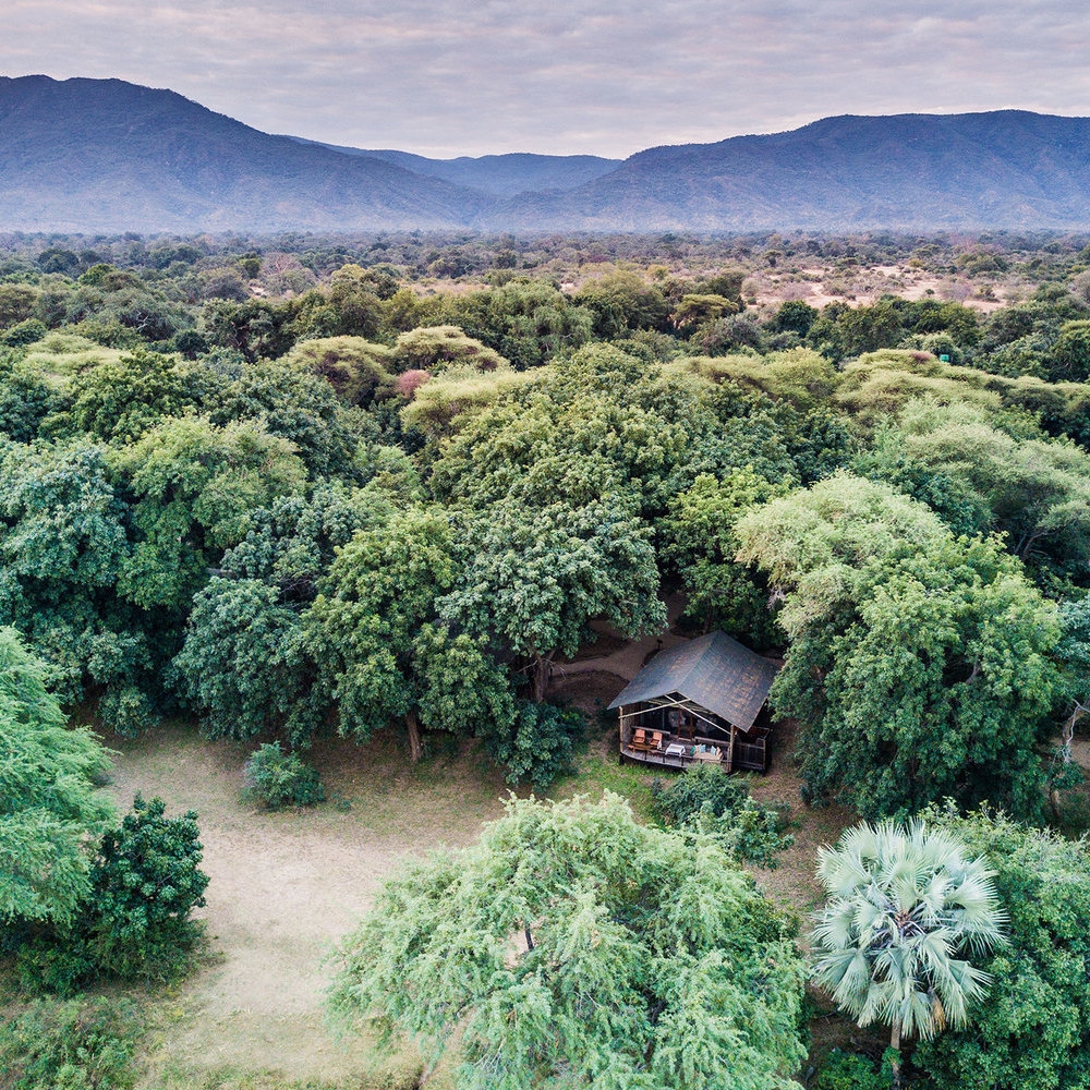 Aerial view of a safari tent surrounded by lush green trees with mountains in the background at Chiawa Camp.
