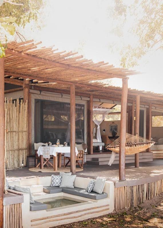 Covered safari tent deck featuring a sunken seating area, a dining table set for two, and a woven hammock.