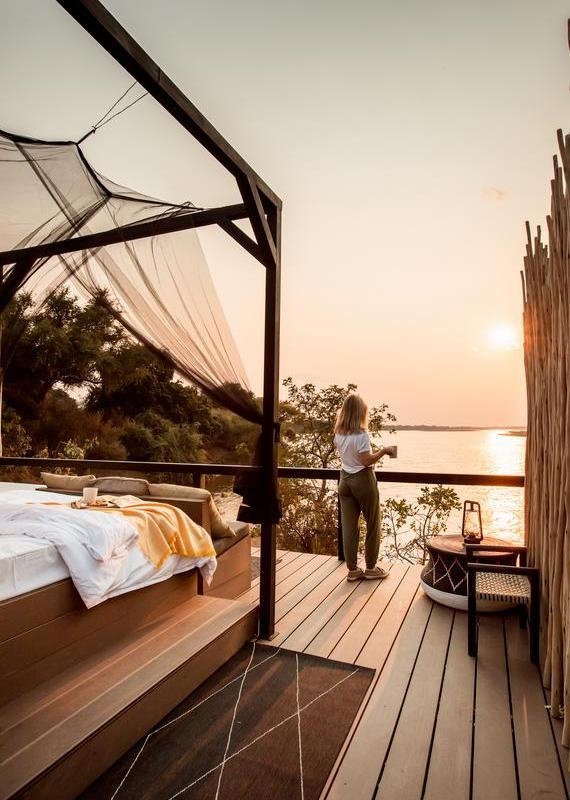 View from an outdoor bed with mosquito netting and a breakfast tray, looking over a wide river at sunrise.