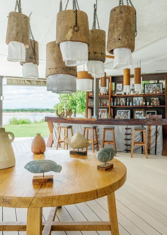 Open-air bar with wooden stools, hanging rustic lights, and a foreground table displaying two stone fish sculptures.