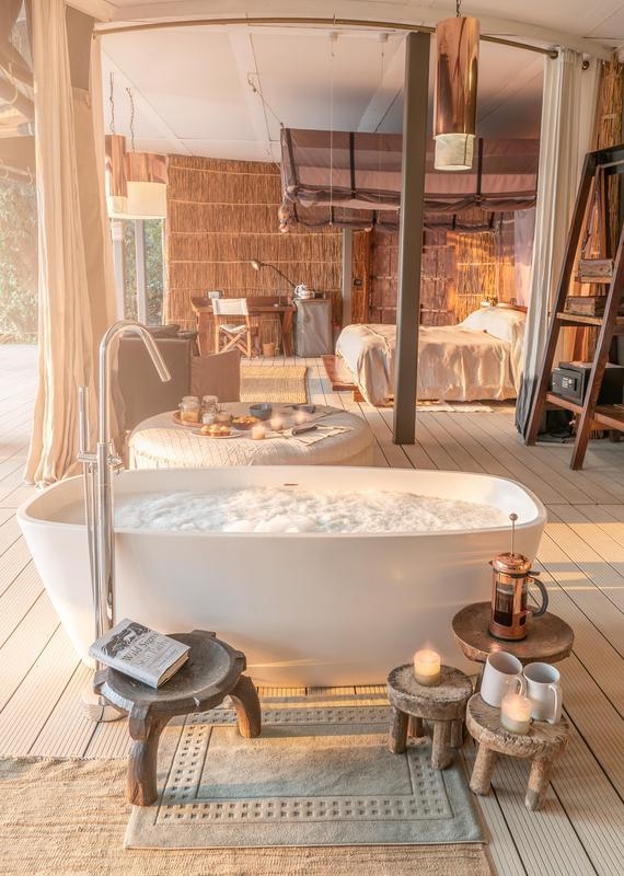 Luxury tent interior featuring a freestanding bathtub, candles, and a stool holding a book titled Wild Signs Star Paths.