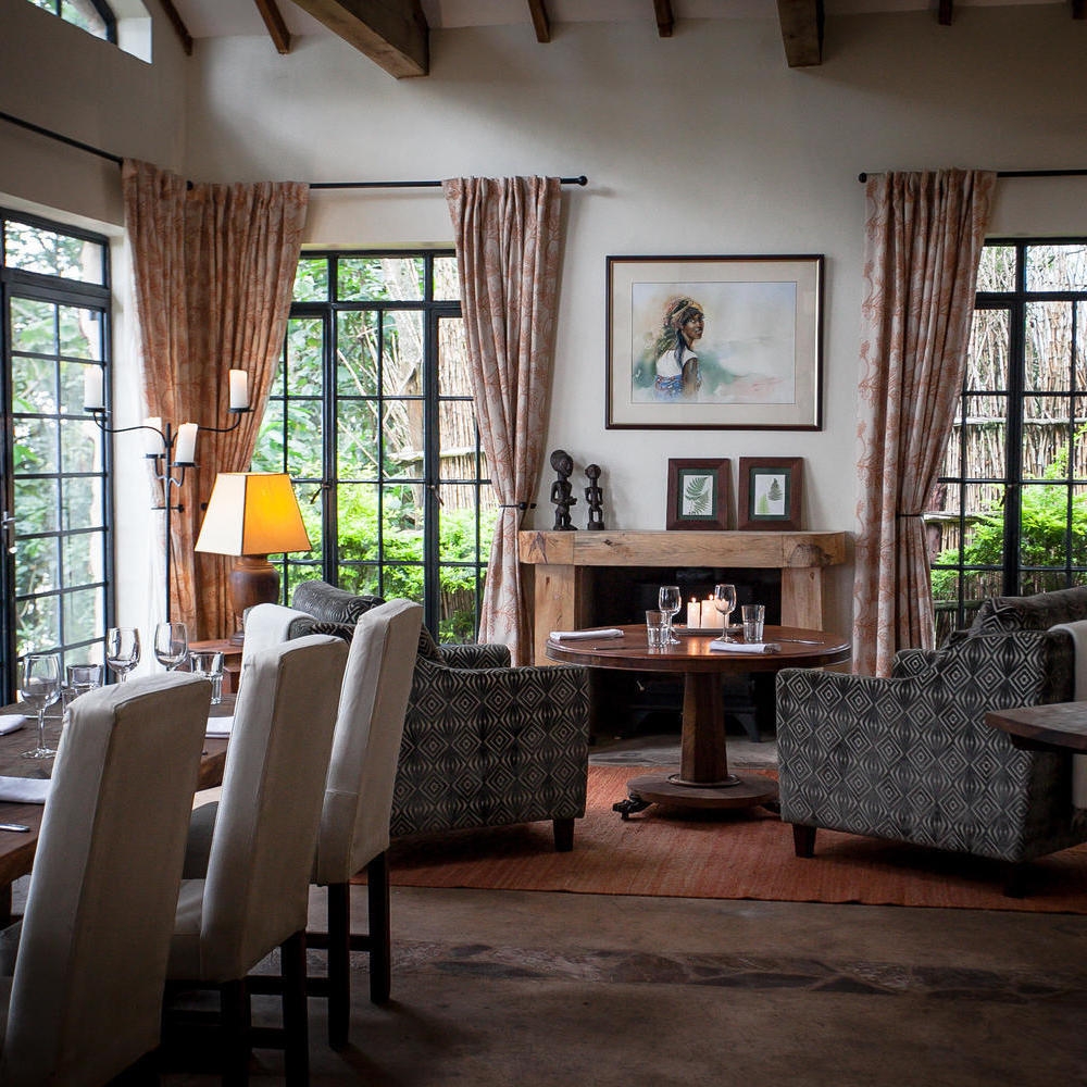 Elegant dining room at Clouds Lodge Uganda with a set wooden table, white chairs, and large windows.