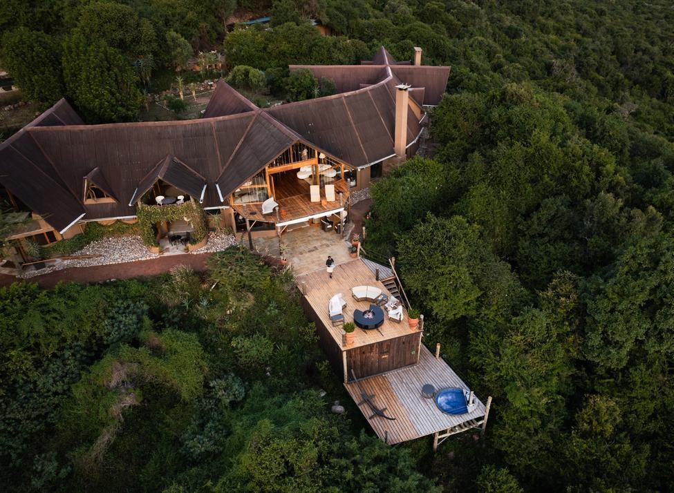 Aerial view of Cottar's Bush Villa, a multi-level lodge with a brown roof and tiered wooden decks amid lush forest.