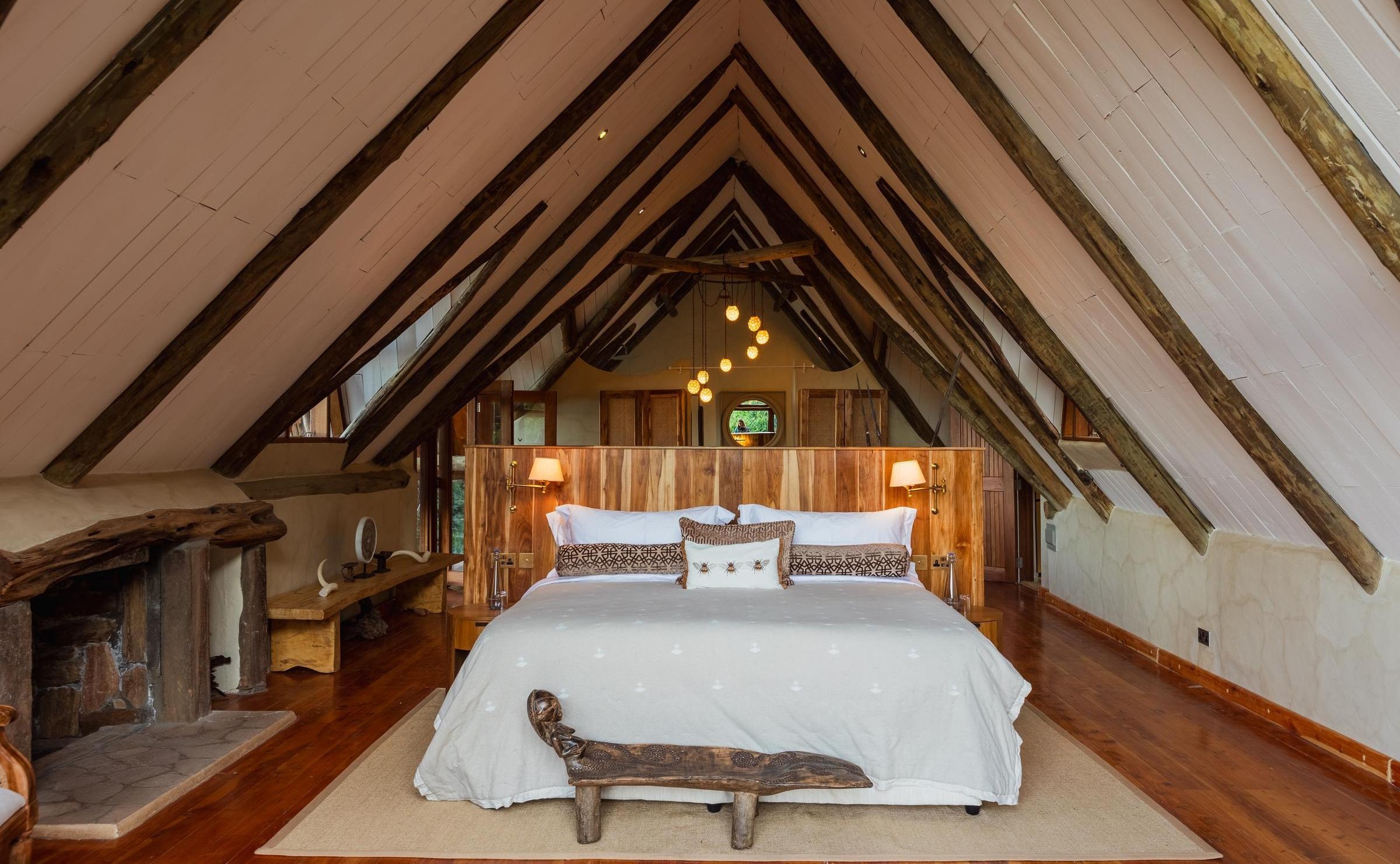 Bedroom with a steep A-frame wooden roof, a large bed with a wooden headboard, and a stone fireplace.