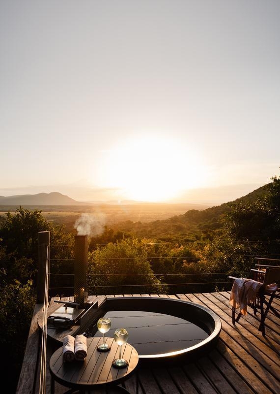 Outdoor round plunge pool with a wood-fired heater on a wooden deck, alongside two drinks, overlooking a valley at sunset.