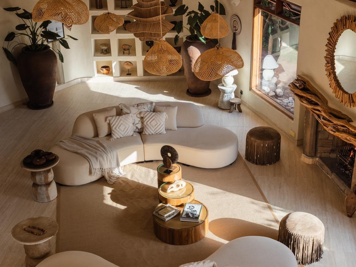 High angle view of a lounge with a curved white sofa, round wood tables, woven pendant lights, and large clay pots.