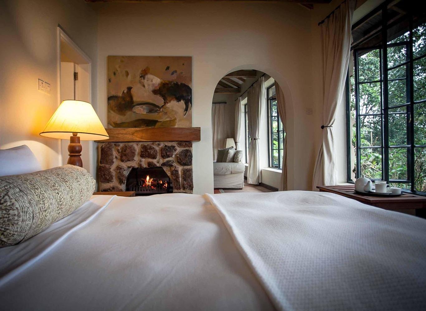 Bed with white linens facing a lit stone fireplace in a cozy room at Clouds Lodge Uganda.