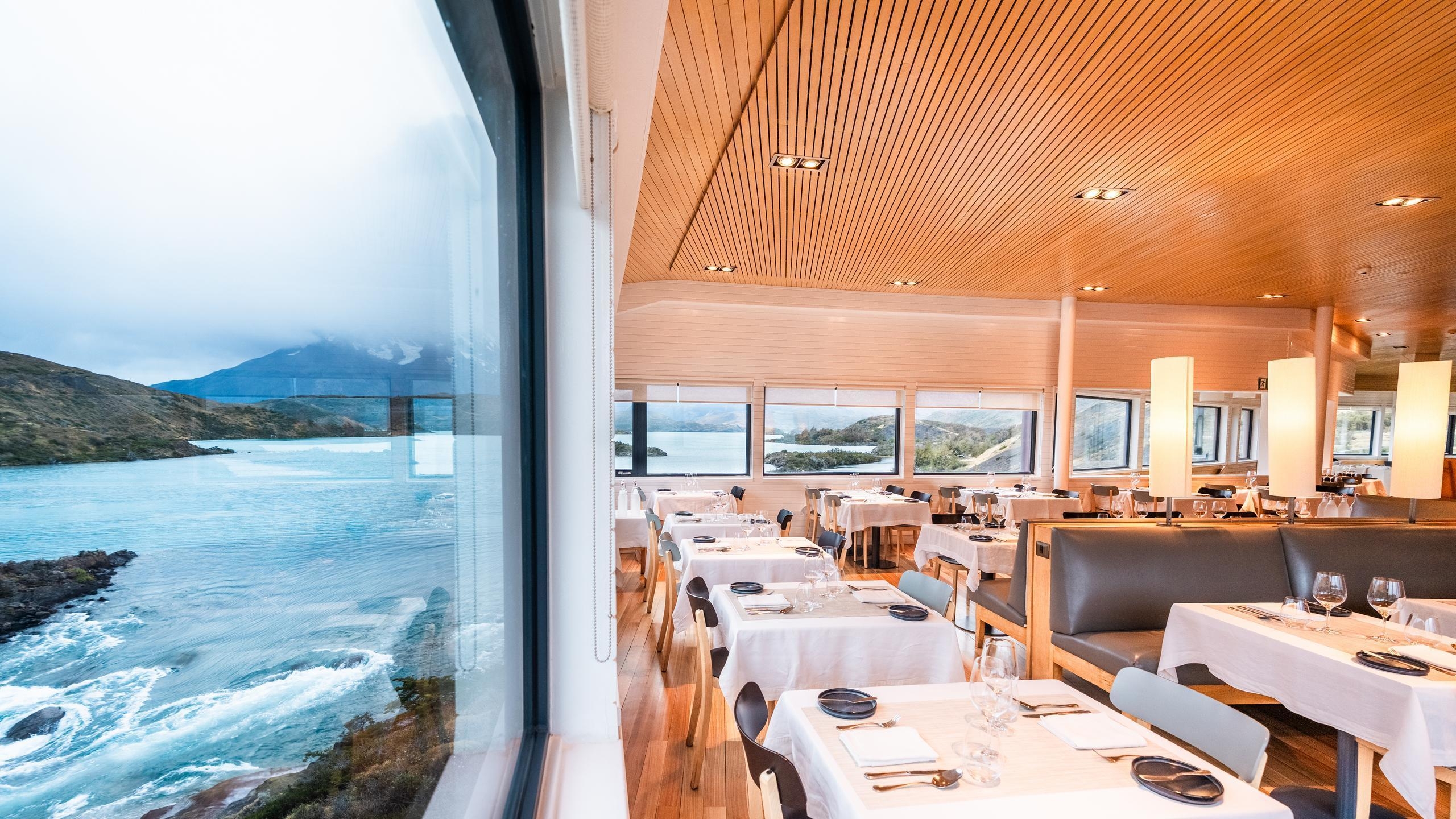 Explora Patagonia dining room with exposed wood beams, set tables, and a large red indoor fireplace.