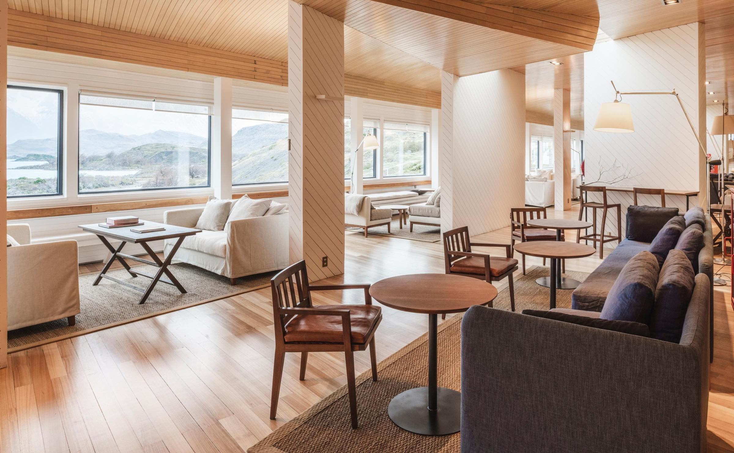 Sunlit Explora Patagonia seating area with white armchairs, small dark tables, and wood floors.