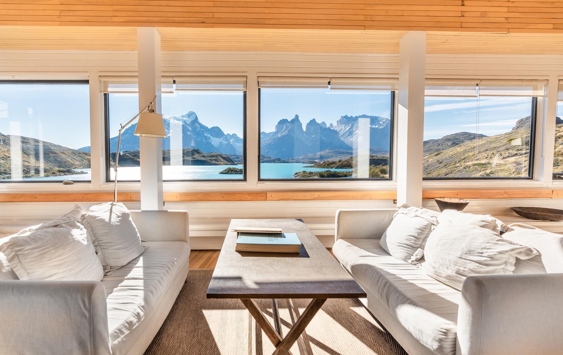 Large Explora Patagonia lodge interior featuring wooden floors, various couch setups, and windows showing the landscape.
