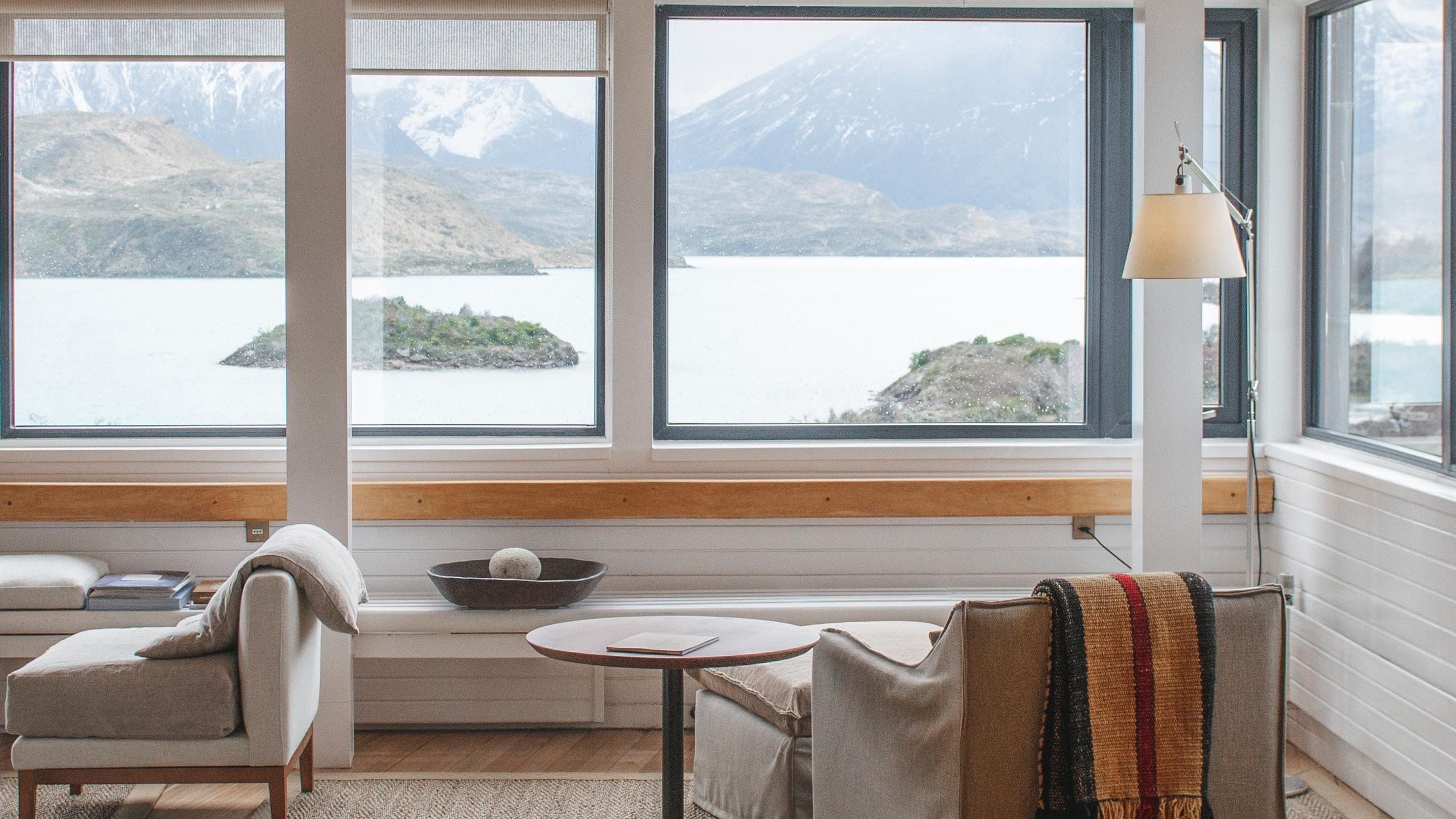 A modern hotel seating area with large glass windows looking out over a wide lake and mountains at Explora Patagonia.