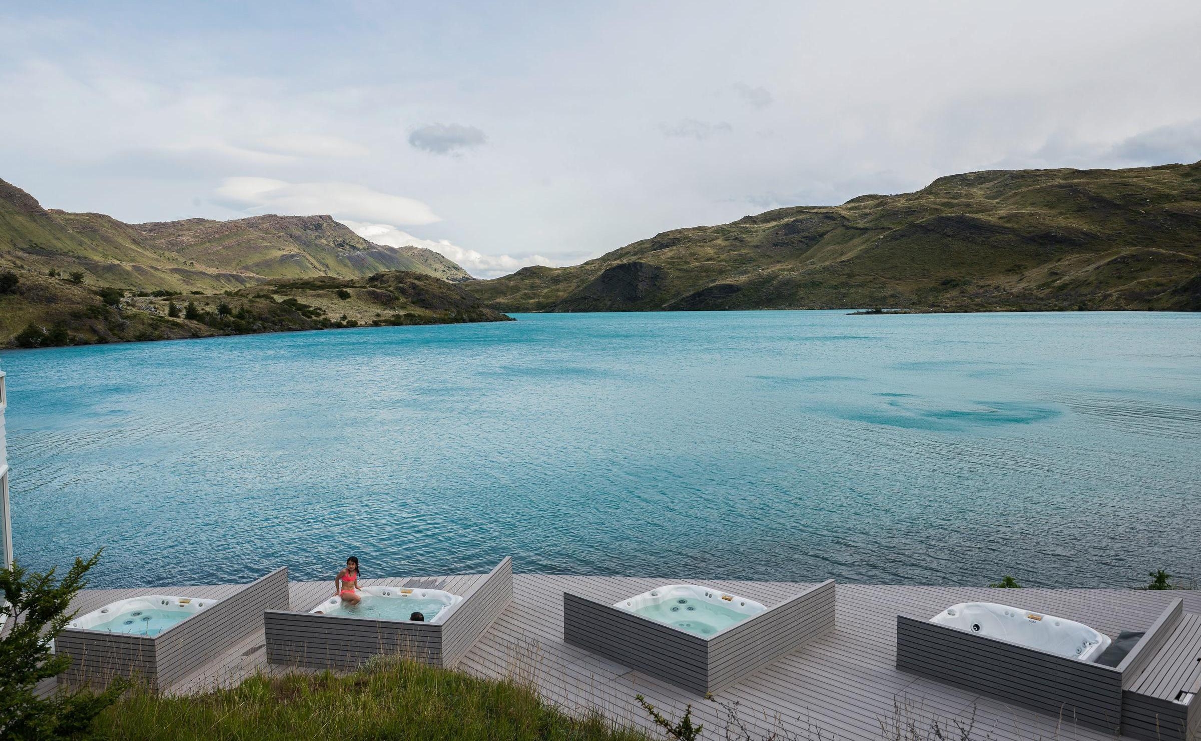 Outdoor hot tubs built into a wooden deck overlooking a vibrant turquoise lake at Explora Patagonia.