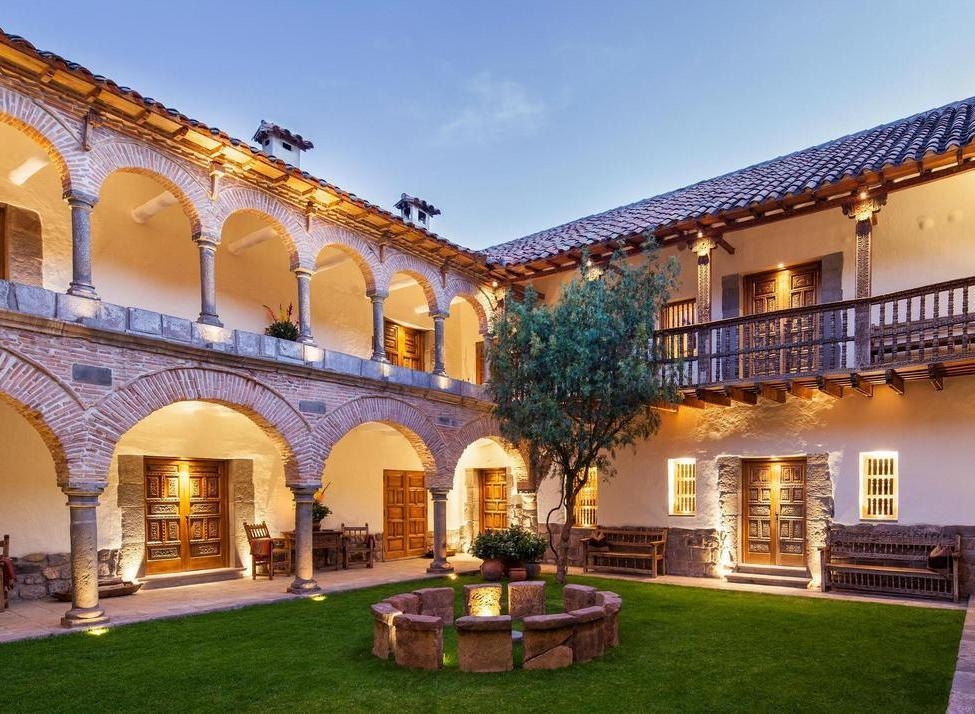 An illuminated colonial courtyard with stone archways, a green lawn, and wooden balconies at Inkaterra La Casona.