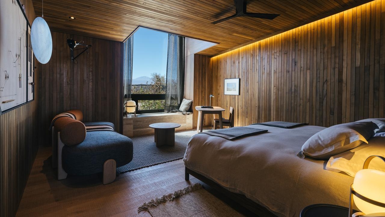 Hotel room with wood paneling, a large bed, modern seating, and a large window looking out at a desert landscape.