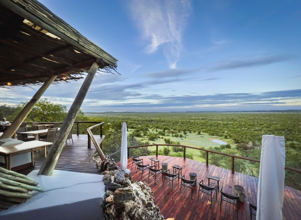 Wooden outdoor viewing deck at Ongava Lodge with chairs overlooking an expansive green savanna landscape.
