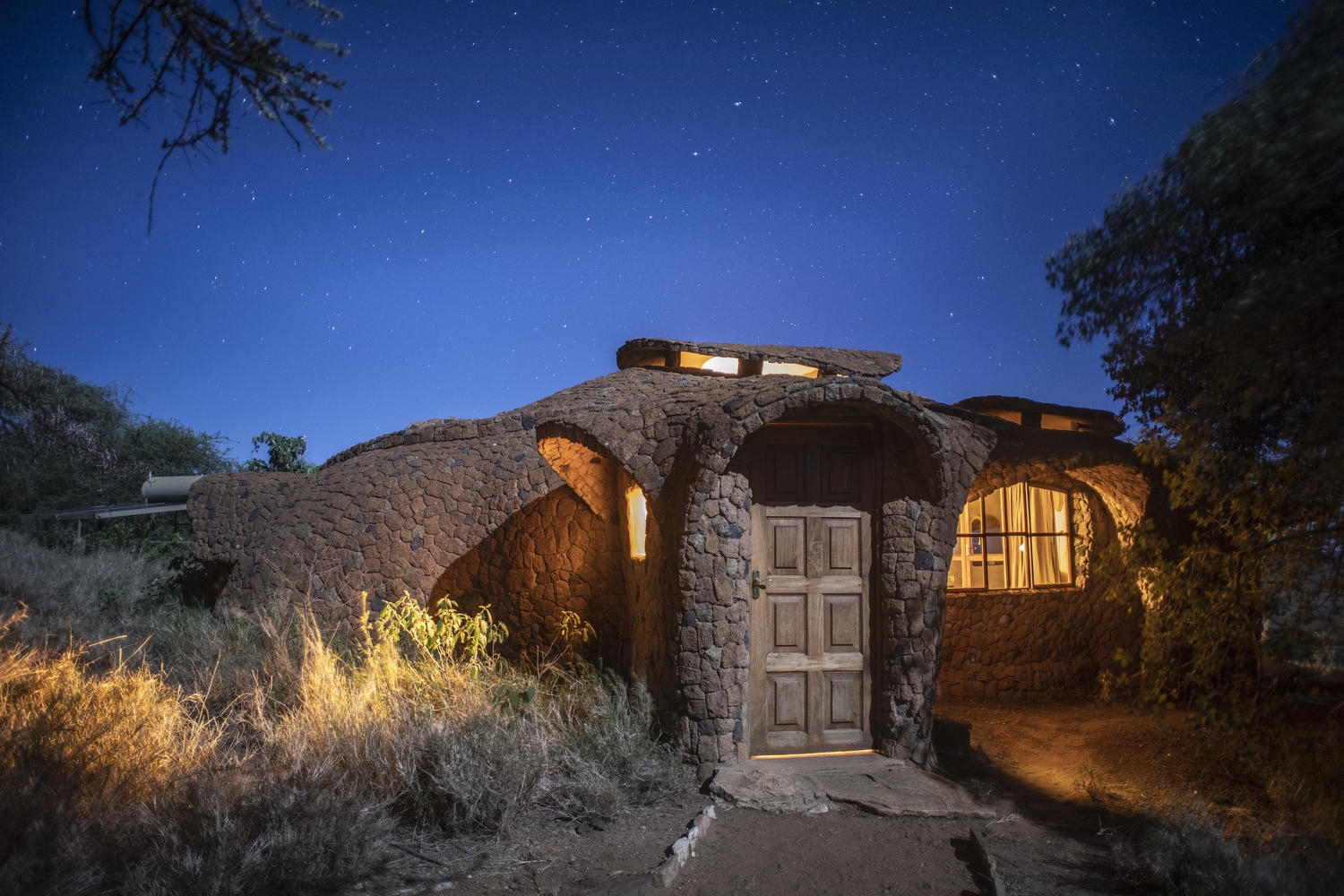A unique stone cottage with a wooden door illuminated at night under a clear sky filled with stars.